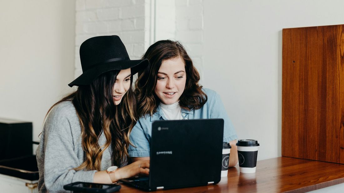 Two young founders sharing a laptop and takeaway coffees while checking their business numbers