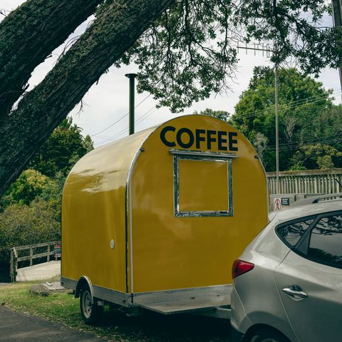 A yellow mobile coffee trailer parked near an Auckland beach
